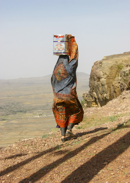 Yemeni woman carrying a bucket of water on her head, Al Mahwit Governorate, Kawkaban, Yemen