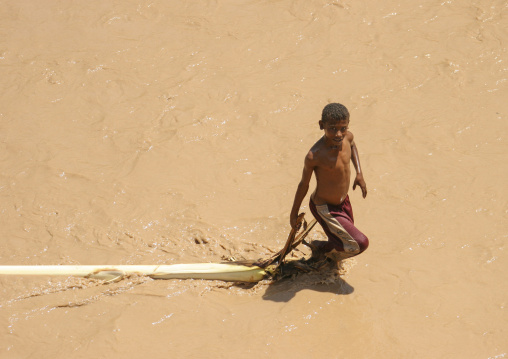 Yemeni boy pulling a palm tree in a muddy river, Thiama, Wadi Mawr, Yemen
